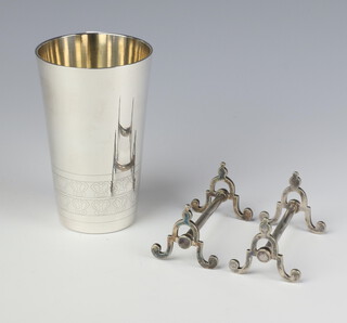 A silver beaker with engraved decoration London 2002, 11cm, 242 grams, maker Garrards, together with a pair of plated knife rests 