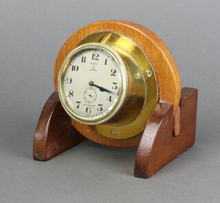 Astral, a 1930's 8 day yacht/aircraft clock with 7cm silvered dial, Arabic numerals, contained in a brass case with winding bezel and hands adjustment, raised on a later oak stand 