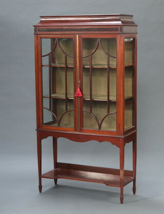 An Edwardian inlaid mahogany display cabinet with shaped top, fitted shelves enclosed by astragal glazed panelled doors, the base fitted an undertier, raised on square tapered supports 170cm h x 90cm w x 34cm d 