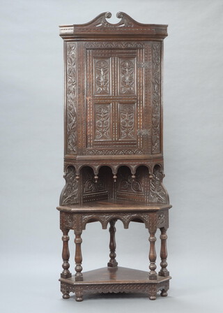 A Victorian heavily carved oak corner cabinet, the upper section with shaped cornice fitted shelves enclosed by a panelled door above a recess, the base with undertier and on bun feet 221cm h x 91cm w x 61cm d 