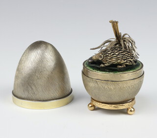 A Stuart Devlin silver gilt surprise egg, the textured body with a plain girdle opening to reveal a hedgehog beneath a bush, on a green and enamelled base, hallmarks to base London 1978, no.149, 134 grams, 7cm 