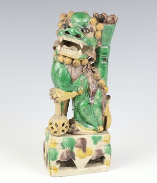 A 19th Century Qing Dynasty slip glazed figure of a buddhistic lion joss stick holder, with reticulated eyes, seated with his left front paw raised above a rising brocade ball, on a rectangular base 20cm h 