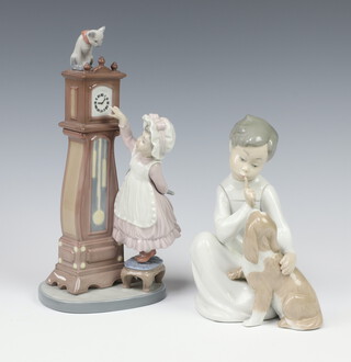 A Lladro figure of a boy with puppy 4522 19cm together with 1 other of a girl with longcase clock 5847 25cm 