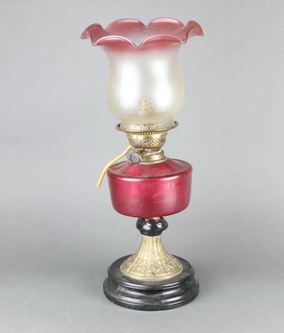 A Victorian oil lamp with cranberry glass reservoir, raised on an embossed metal base, the knop with crude repair complete with associated etched glass shade 33cm h, converted to electricity 