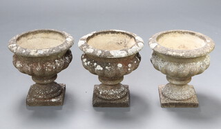 Three well weathered concrete garden urns with lobed bodies, raised on square feet 41cm h x 41cm diam. 