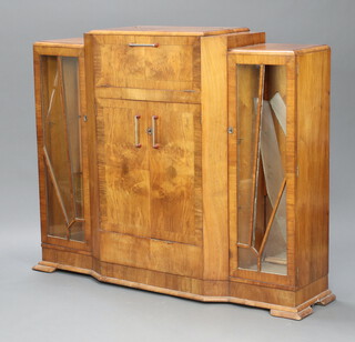 A 1930's Art Deco figured walnut cocktail display cabinet, the centre section with hinged lid, the interior fitted glass recepticals, base with cupboard fitted bottle receptacles flanked by cupboards enclosed by astragal sunburst style doors 121cm h x 145cm w x 39cm d  