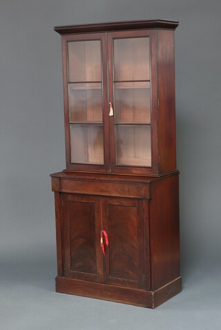 A Victorian mahogany bookcase on cabinet with moulded cornice the upper section fitted shelves enclosed by glazed panelled doors, the base enclosed by panelled door, raised on a platform base 197cm h x 84cm w x 46cm d 