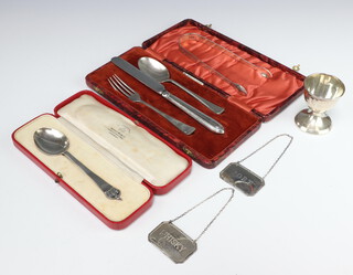 A weighted silver egg cup Birmingham 1931, a pair of sugar nips, 2 silver spirit labels, a cased set of cutlery and a cased dessert spoon, weighable silver 103 grams