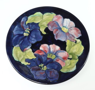 A Walter Moorcroft blue ground plate decorated clematis pattern, monogrammed and with paper label 30cm 