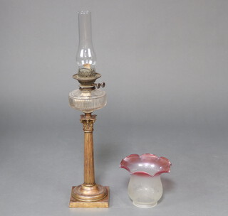 A reeded gilt metal oil lamp with Corinthian column and faceted glass reservoir, chimney and red glass shade 50cm h x 15cm x 15cm 