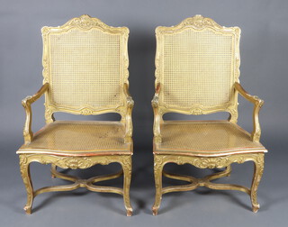 A pair of 19th Century French gilt painted open arm salon chairs with woven cane seats and backs, raised on cabriole supports with X framed stretchers 113cm h x 65cm w x 49cm d (seats 35cm x 33cm)  