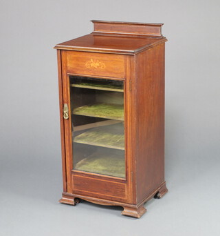 An Edwardian inlaid mahogany music cabinet with raised back inlaid musical trophies, fitted shelves enclosed by a glazed panelled door, raised on bracket feet 97cm h x 38cm w x 41cm d  