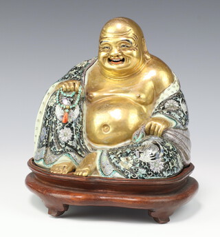 A famille verte figure of Budai, late Qing dynasty/Republican period, the seated figure with open mouth and visible teeth painted in gilt and his ornate robe decorated with phoenix and lotus, impressed mark to the base - seal of Xue Wei Sen (probably the maker) raised on a wooden stand, 19cm h