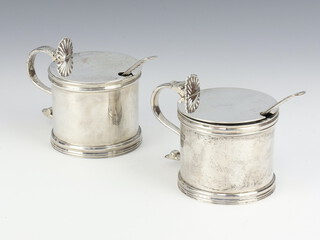 A near pair of Georgian design mustards with shell thumb pieces, spoons and blue glass liners, rubbed marks, 306 grams