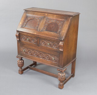 An Edwardian carved oak bureau, the fall front revealing a well fitted interior above 2 drawers, raised on cup and cover supports with H framed stretcher 96cm h x  87cm w x 45cm d 