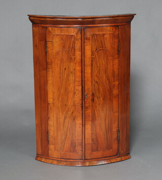 A Georgian inlaid walnut bow front hanging corner cabinet with moulded cornice, fitted shelves enclosed by panelled door 93cm h x 66cm w x 45cm d  