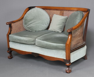 A 1930's carved walnut single cane bergere suite comprising 2 seat sofa 78cm h x 125 cm w x 70cm d (seat 110cm w x 48cm d) and 2 matching armchairs 78cm h x 63cm w x 64cm d (seats 41cm x 34cm) all with blue loose cushions, raised on cabriole supports 