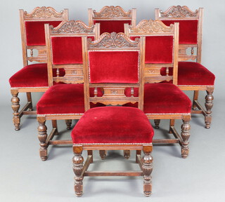 A set of 6 Edwardian carved oak show frame dining chairs the seats and backs upholstered in red material, raised on cup and cover supports 94cm h x 47cm w x 46cm d 