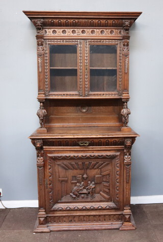 A 19th Century Dutch carved oak display cabinet on cabinet with moulded cornice and lion ring masks, decorated with a pair of standing musicians, the base fitted 1 long drawer enclosed by a carved panelled door depicting a knife fight at an inn 210cm h x 104cm w x 56cm d 