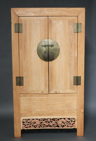 A 19th Century Chinese bleached hardwood cabinet enclosed by a pair of panelled doors with circular gilt metal panel and pierced carved apron 208cm high x 115cm w   x 57cm d 