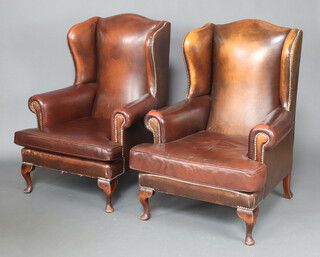 A pair of Georgian style wing armchairs upholstered in brown leather, raised on cabriole supports 112cm h x 79cm w x 78cm (seats 32cm x 49cm) 