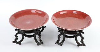 A matched pair of early 20th Century Chinese copper red shallow dishes on wooden stands 14.5cm  