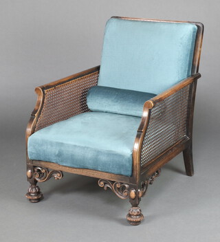 A 1930's beech framed single cane bergere armchair upholstered in blue material, raised on turned supports 89cm h x 69cm w x 70cm d 