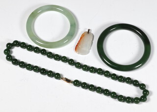 A dark green hardstone bangle 7cm diam., a pale green ditto 8cm, a dark green bead necklace 44cm and a carved pendant 4cm 