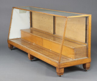 A 1930's Art Deco oak and plate glass wedge shaped shop display cabinet with stepped interior, raised on square supports 94cm h x 213cm w x 62cm d 