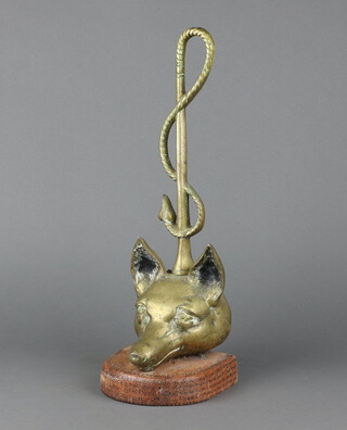 A brass door stop in the form of a foxes mask with whip handle, raised on an oval pine base 42cm x 11cm x 12cm 