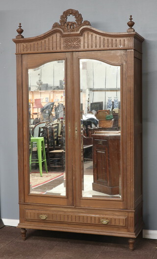 A 19/20th Century French bleached oak armoire with arched top, the interior with hanging space, the base fitted a drawer, enclosed by a pair of bevelled plate mirror panelled doors 239cm h x 129cm w x 47cm d 