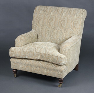 A Howard style armchair upholstered in light coloured paisley style material, raised on turned supports 92cm h x 86cm w x 78cm d 