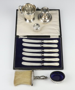 A silver mug with presentation inscription Birmingham 1913, a dwarf candlestick, mustard, toilet jar and mounted brush, and 6 mother of pearl butter knives, weighable silver 76 grams 