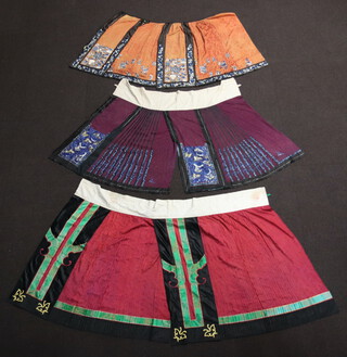Three Late Qing Dynasty Chinese Han style silk damask skirts including, a purple skirt with 2 half panels embroidered blue flowers with moths the pleats embroidered flowers 92cm long ,a red pleated skirt  with green and gold borders, embroidered gold butterflies and plants 95cm long and an orange skirt with diamond pleats and black border (missing waistband) the panels embroidered flowers in vases and the border embroidered flowers 78cm long