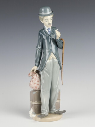 A Lladro figure of a standing Charlie Chaplin with suitcase sack and walking cane, 28cm 