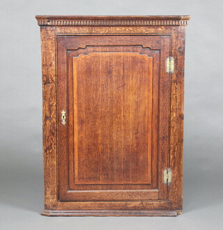 A Georgian oak corner cabinet with moulded and dentil cornice, fitted shelves enclosed by a panelled door with brass H framed hinges 107cm h x 79cm w x 56cm d 