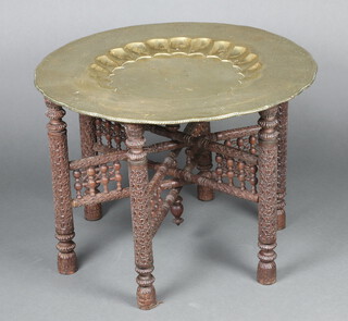 A circular Benares brass charger raised on a carved hardwood folding stand 58cm h x 78cm