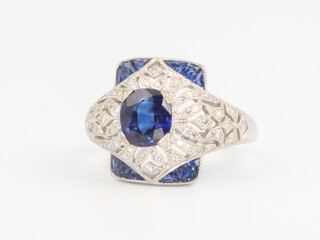 A white metal Edwardian style sapphire and diamond cocktail ring set with an oval sapphire surrounded by diamonds with sapphire corners, diamonds 0.28ct, sapphires 1.05ct, 6 grams, size M 1/2 THIS LOT IS WITHDRAWN FROM THE AUCTION 