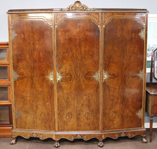 A 1930's Italian style walnut triple wardrobe with carved crest to the centre, the centre fitted 3 trays above 3 drawers and having a rectangular plate mirror, flanked by hanging spaces enclosed by panelled doors with gilt metal embellishments throughout, raised on scrolled cabriole supports 207cm h x 196cm w x 69cm d 