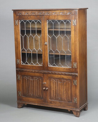 A carved oak display cabinet/bookcase case, fitted shelves enclosed by lead glazed panelled doors, the base enclosed by linenfold panelled doors 135cm h x 94cm w x 32cm d 