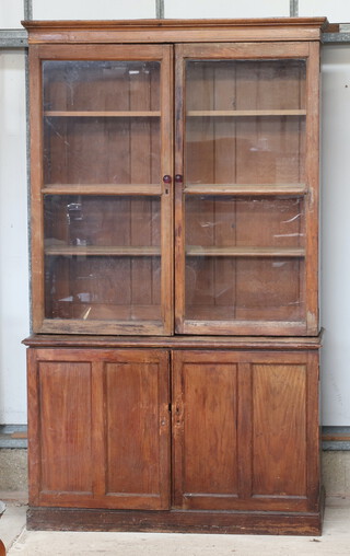 A 19th Century  pine cabinet on cabinet with moulded cornice, fitted shelves enclosed by glazed panelled doors, the base enclosed by panelled doors, on a platform base 213cm  h x 128cm w x 41cm d 