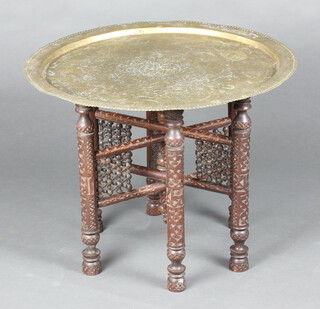 A circular engraved Eastern tray raised on a folding hardwood stand 49cm h x 64cm diam. 