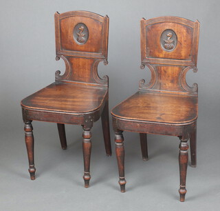 A pair of Georgian mahogany slat back hall chairs, the shaped backs with carved armorial and solid seats, raised on turned supports 86cm h x 44cm w x 41cm d (seats 28cm x 28cm) 