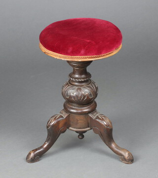 A Victorian carved oak revolving piano stool raised on a baluster carved tripod and base, the seat upholstered in red material 49cm h x 32cm diam.  