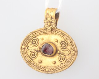 A Roman style oval gold pendant set with a rough cut garnet with Etruscan style decoration 3.5 grams, 25mm diam. 