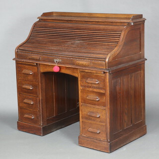 An Edwardian oak roll top desk, the top with 3/4 gallery and well fitted interior, the base fitted 1 long drawer, the pedestals with 2 brushing slides and 8 short drawers 122cm h x 120cm w x 69cm d 