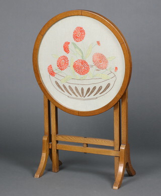 A 1930's Art Deco light oak circular fire screen/occasional table with embroidered top decorated a bowl of flowers, raised on square supports 64cm h x 55cm diam. 