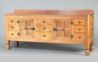 Robert "Mouseman" Thompson of Kilburn, an oak and figured elm sideboard with signature mouse to front right hand support and raised carved adzed back and top, fitted 3 drawers flanked by cupboards enclosed by panelled doors with wrought iron locks, flanked by a further 6 short drawers, raised on octagonal bun feet 85cm h x 183cm w x 46cm d 