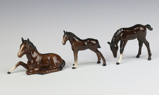 A Beswick figure of a foal lying No 915 brown gloss 8cm together with a ditto  foal grazing No 946 8.3cm and a ditto foal thorough bread type facing left No 1816 9cm all by Arthur Gredington