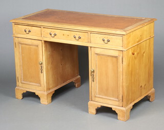 A 19th Century pine desk with brown inset leather writing surface, the frieze fitted 1 long and 2 short drawers, the pedestals fitted cupboards enclosed by panelled doors, raised on bracket feet 77cm h x 120cm w x 60cm d 